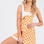 Orange checkered knit romper overalls with cuffed shorts, adjustable straps, and multiple pockets, laid flat to show texture and design.