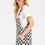 Black checkered knit romper overalls with cuffed shorts, chest and side pockets, and adjustable straps, laid flat to show texture and structure.