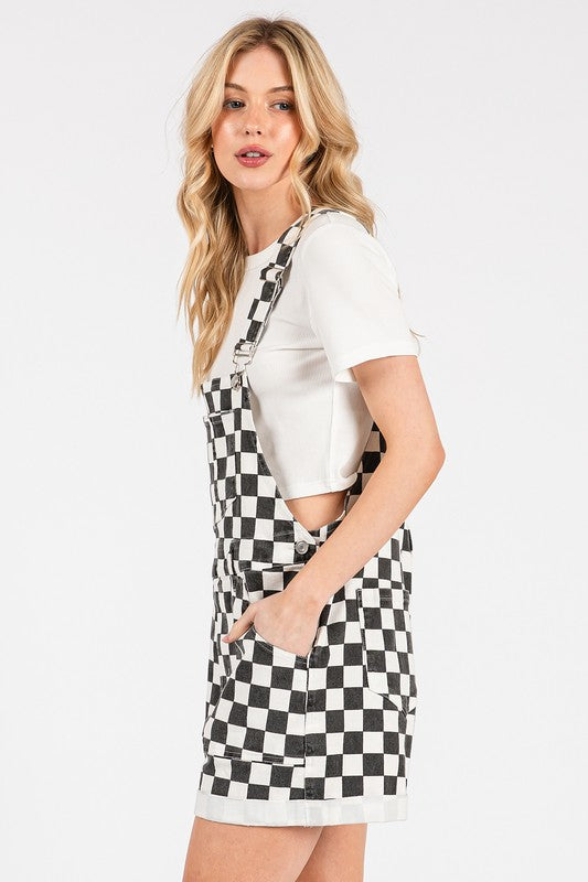 Black checkered knit romper overalls with cuffed shorts, chest and side pockets, and adjustable straps, laid flat to show texture and structure.