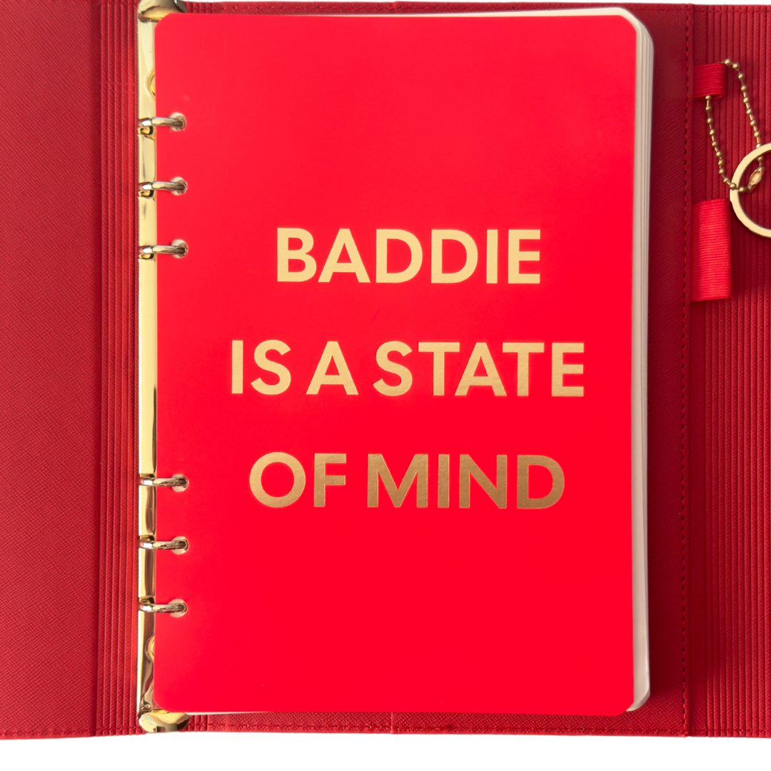 Red notebook with gold text 'BADDIE IS A STATE OF MIND' 