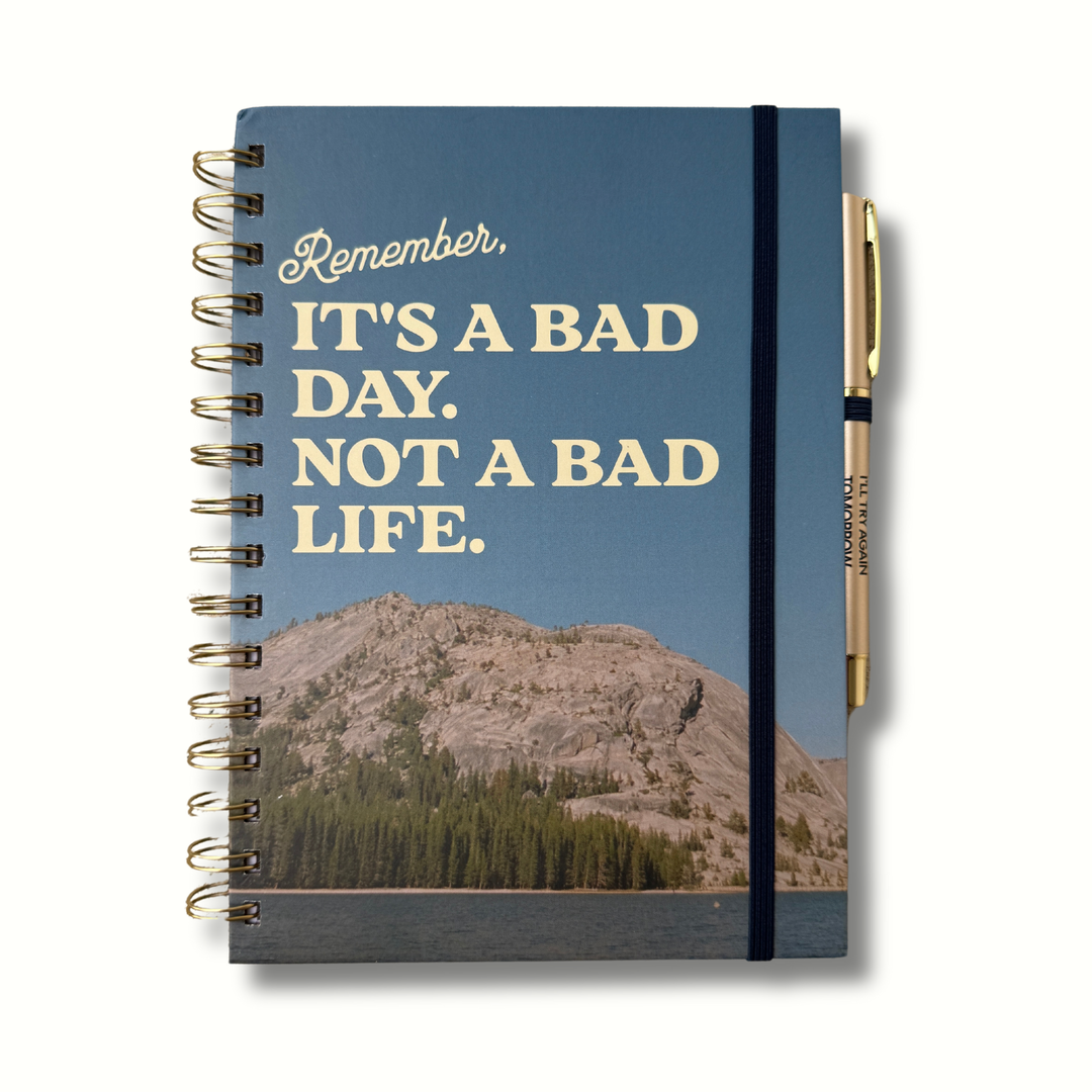Blue hardcover journal with cream lettering that says “It’s A Bad Day. Not a Bad Life.” and features mountains with a lake, matching pen reading “I’ll Try Again Tomorrow,” A5 size, 140 pages.