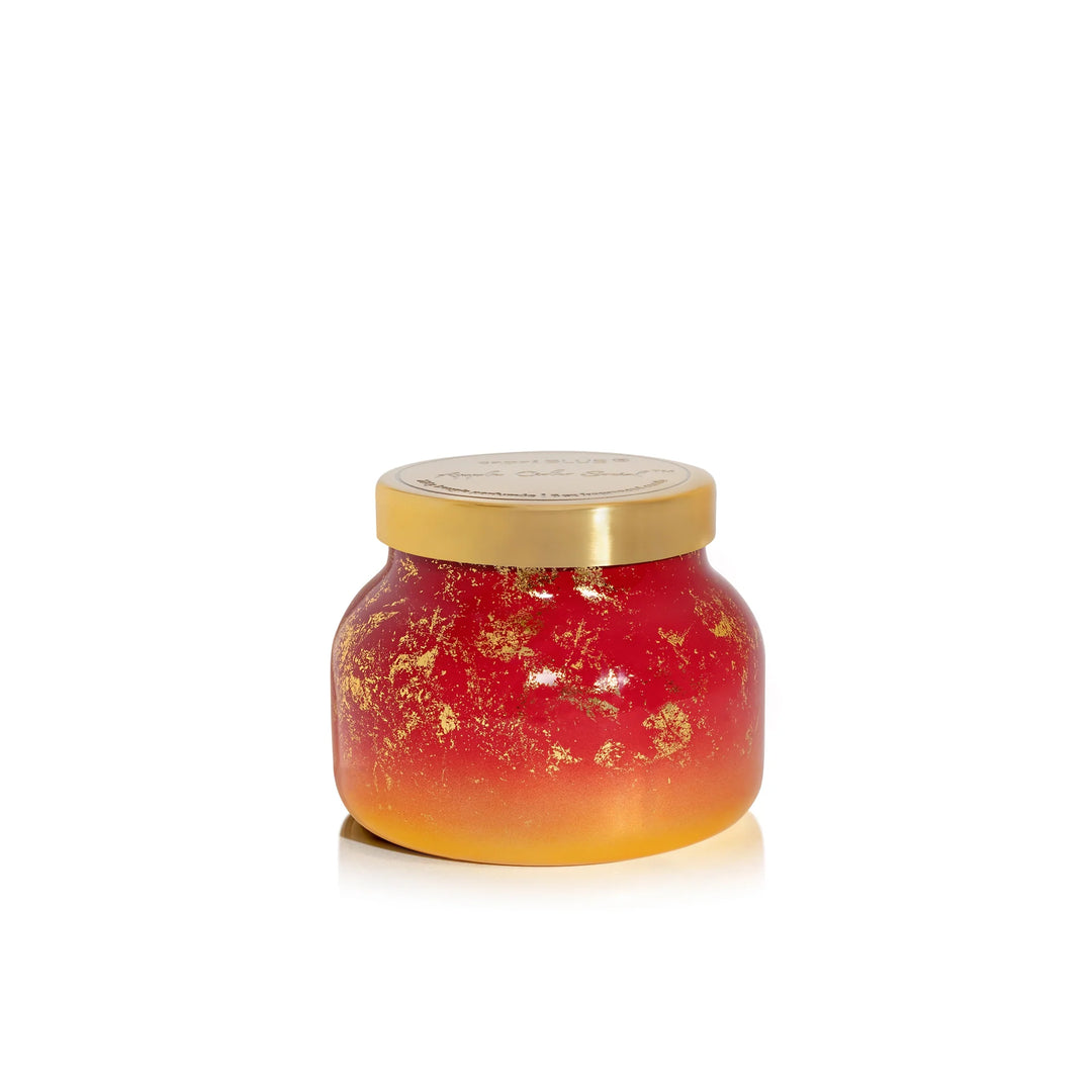 An 8oz Capri Blue Apple Cider Social Glimmer Petite Candle in cranberry red with a metallic finish.