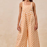 A pair of overalls with an orange and white checkerboard plaid print. The overalls have adjustable straps, front pleats, and a wide-leg silhouette.