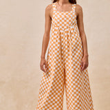 A pair of overalls with an orange and white checkerboard plaid print. The overalls have adjustable straps, front pleats, and a wide-leg silhouette.