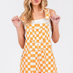 Orange checkered knit romper overalls with cuffed shorts, adjustable straps, and multiple pockets, laid flat to show texture and design.