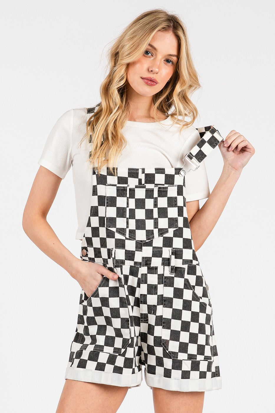 Black checkered knit romper overalls with cuffed shorts, chest and side pockets, and adjustable straps, laid flat to show texture and structure.