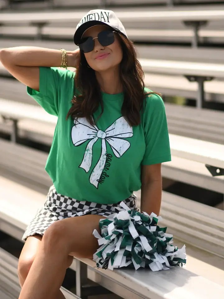 Green Tultex tee with a white bow and bold black “game day” lettering at the bottom, laid flat for display.