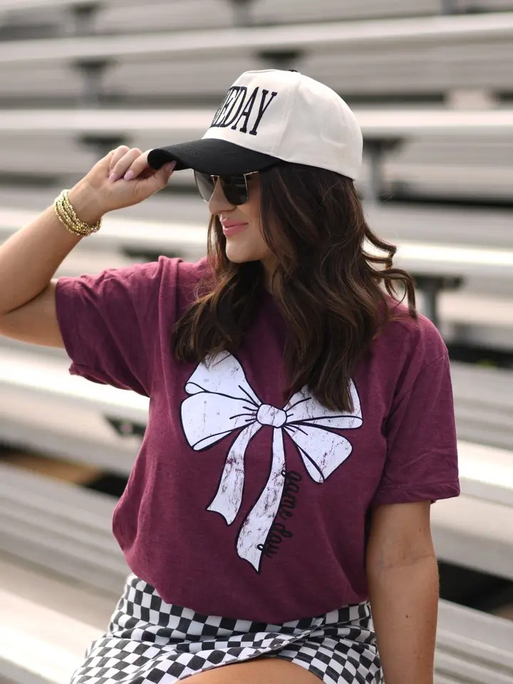 Maroon Tultex tee with a white bow and bold black “game day” lettering at the bottom, displayed flat.