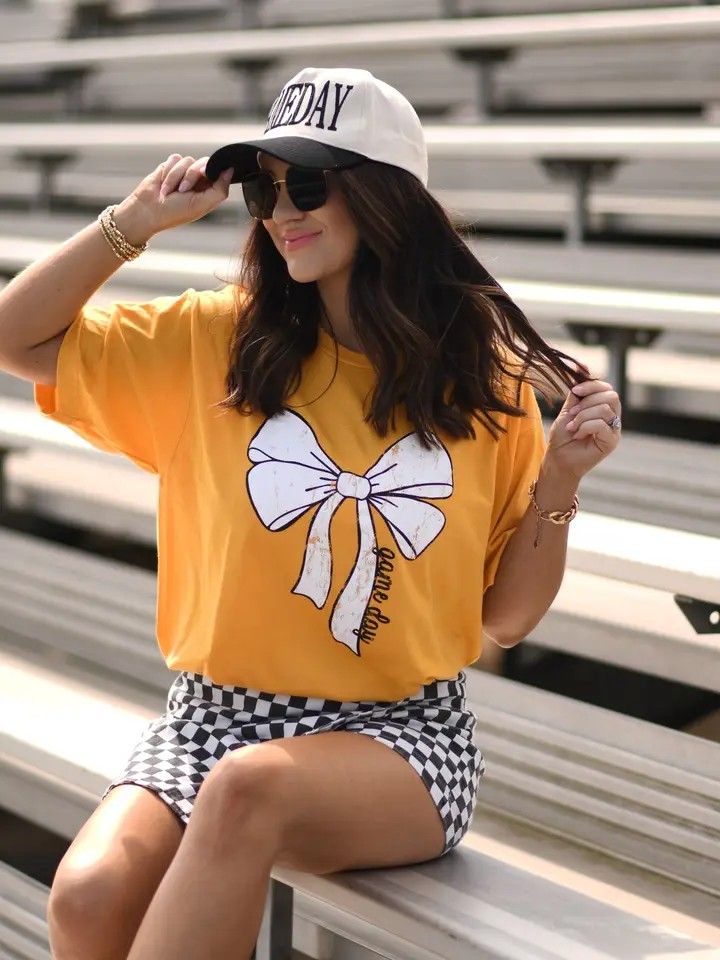 Gold Tultex tee with a white bow and bold black “game day” text at the bottom, displayed flat.