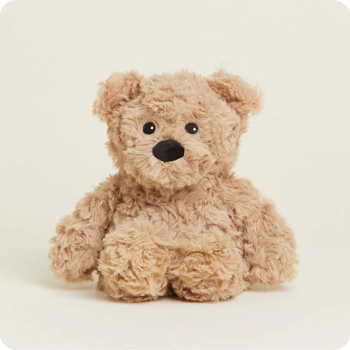 A small, soft plush teddy bear with curly brown fur and a friendly face, designed to be microwavable.